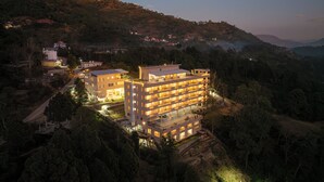 A multi-story hotel with a central courtyard, surrounded by dense forest and hills. - Better Life Homes - For active seniors above 50 years (Solan)