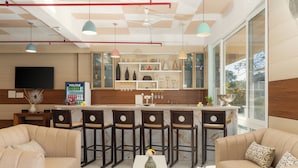 A modern kitchen with bar stools, a central island, and a large window. - Better Life Homes - For active seniors above 50 years (Solan)