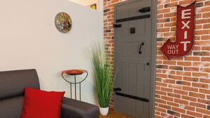Ein modernes Interieur mit grauem Sofa, rotem Kissen, kleinem runden Tisch, Topfpflanze und einer Ziegelwand mit Wegweiserleuchte.