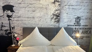 Ein Bett mit zwei weißen Kissen und einem grauen Kopfteil in einem Zimmer mit einer weißen Ziegelwand mit Struktur.