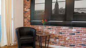 Ein Zimmer mit einer Ziegelwand, einem schwarzen Ledersessel, einem kleinen runden Tisch mit Blumenvase und einem roten Teppich.