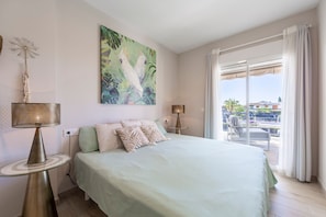 A hotel room with a bed, a side table, a lamp, a painting, and a view of the outside. - Magna Vera, new, bright and family-friendly accommodation. (Vera playa)