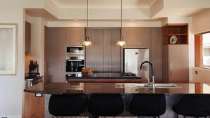 A modern kitchen with a central island, two pendant lights, stainless steel appliances, and a built-in oven.