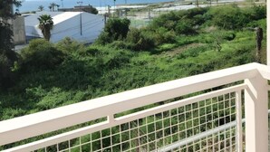 A balcony with a view of a coastal landscape, including greenery and a distant shoreline.