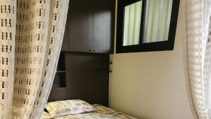 Een slaapkamer met een bed, gordijnen, een raam en een kledingkast.