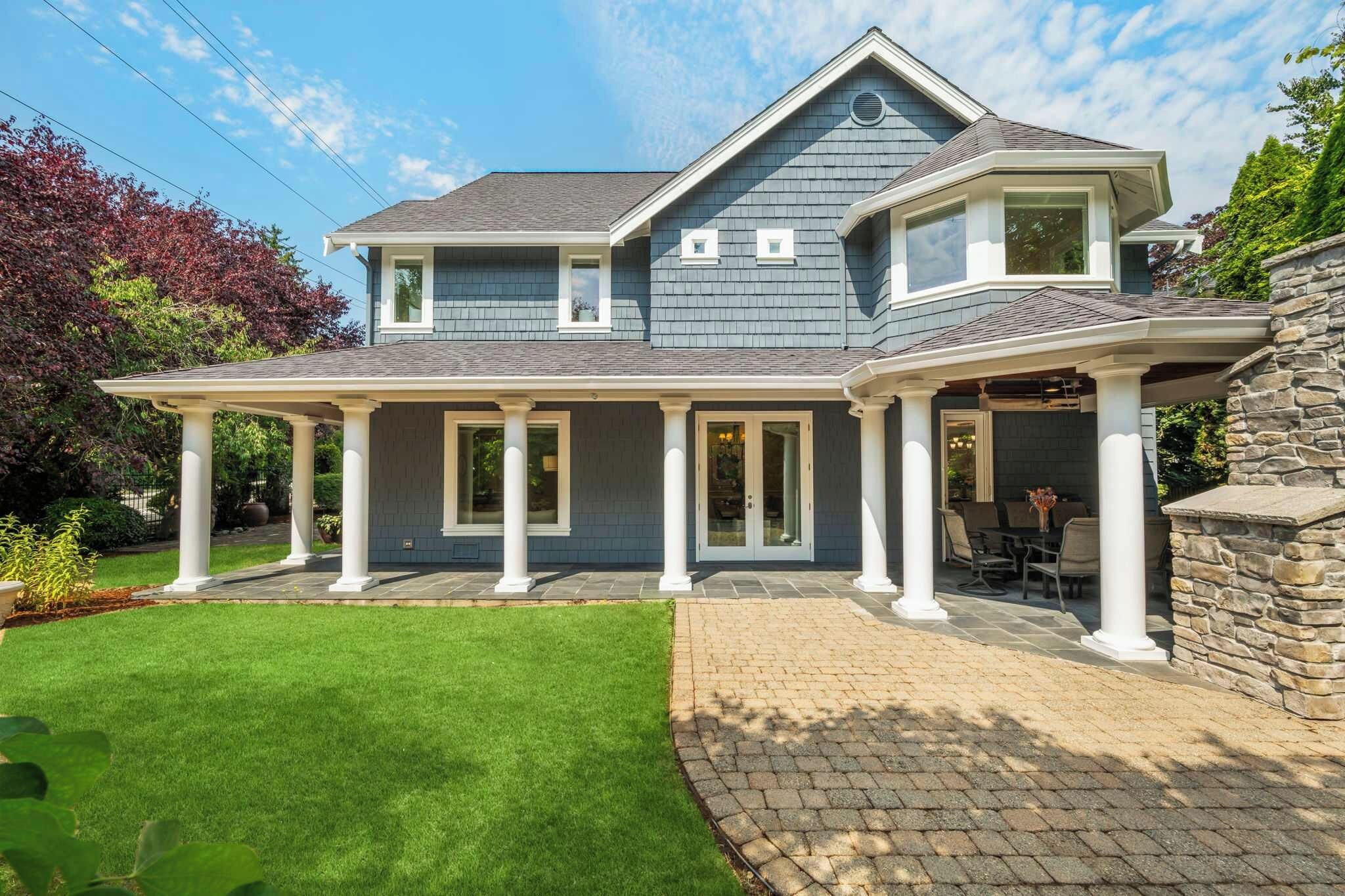 A two-story house with a covered patio and a stone wall.