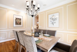 A dining room with a wooden table, upholstered chairs, a chandelier, framed artwork, and a 'FEAT DRINK ENJOY' sign.