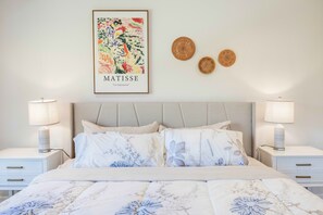 Quarto bem arrumado com uma cama, duas mesas de cabeceira, um encosto e uma obra de arte na parede.