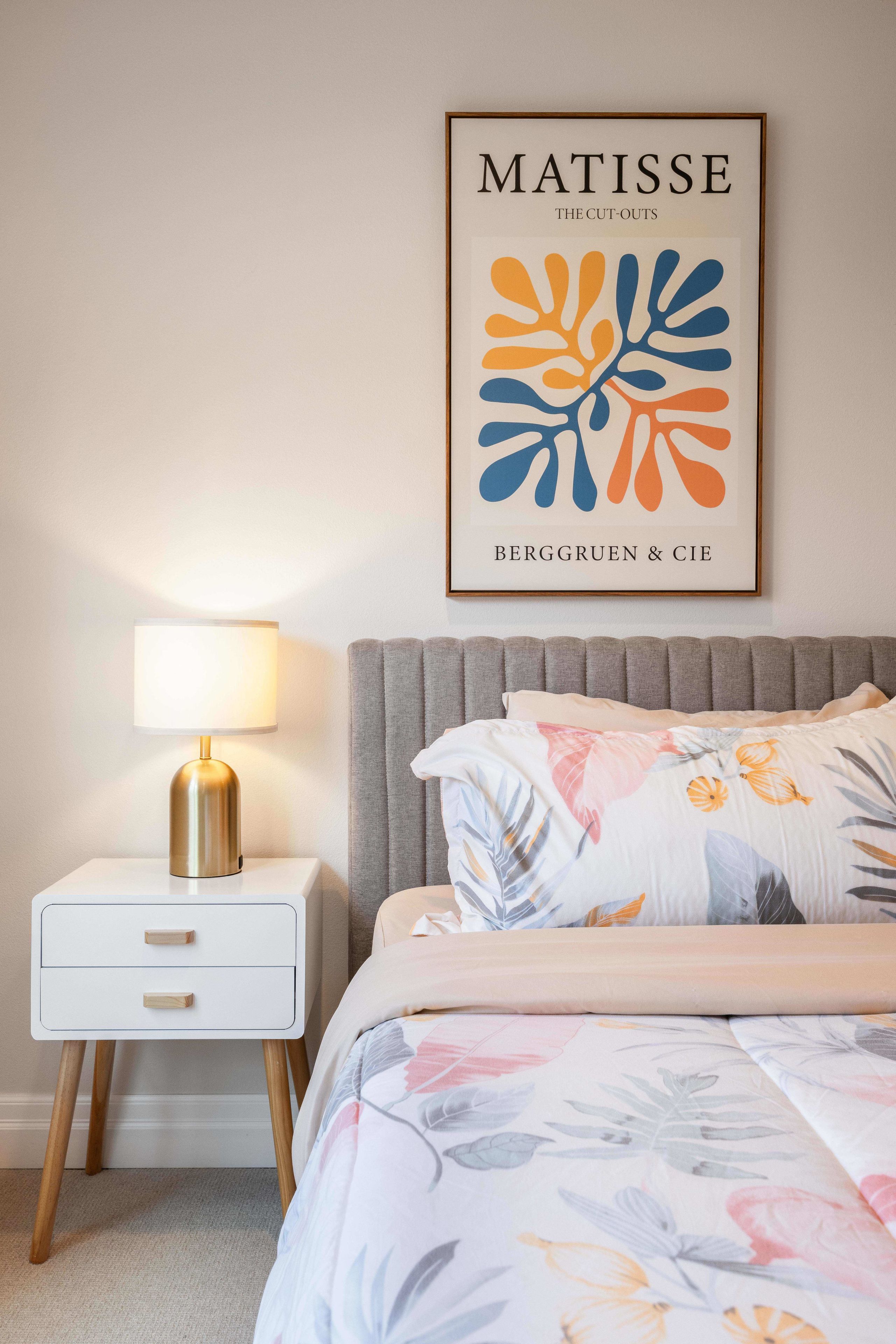 A bedroom with a bed, a nightstand, a lamp, and a framed artwork on the wall.