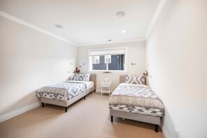 Un dormitorio con dos camas, una mesita blanca y una ventana con persianas.