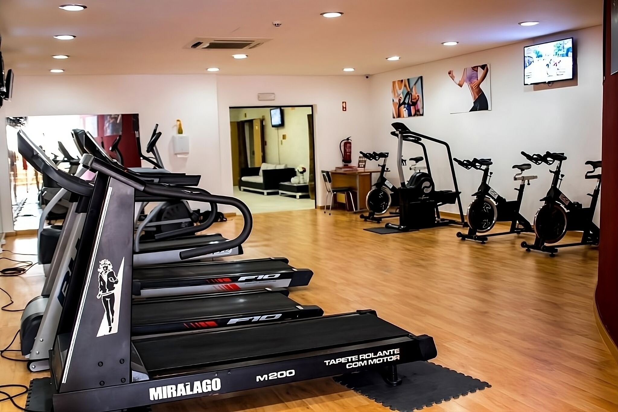 A gym with treadmills, stationary bikes, and a TV on the wall.