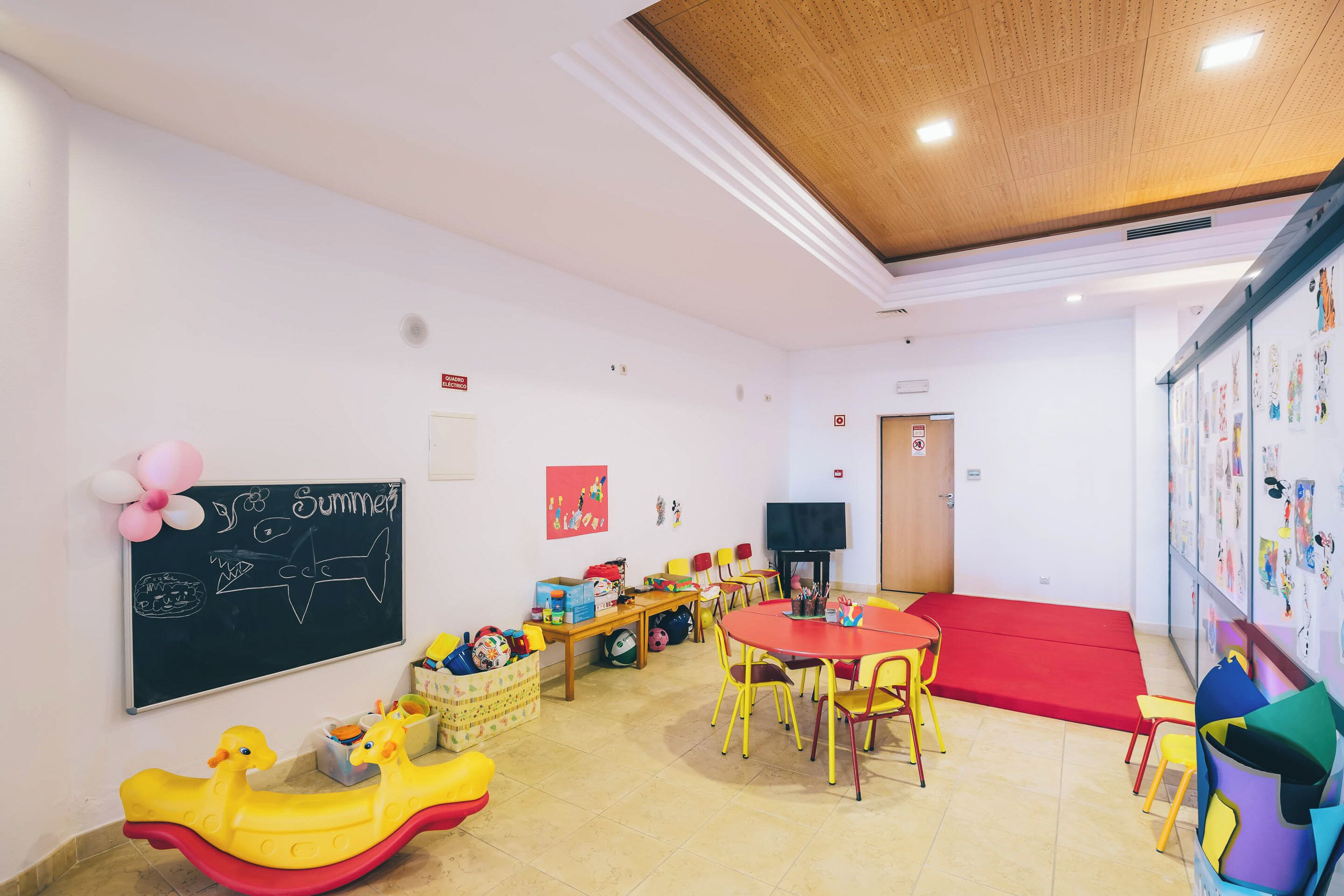 A children's playroom with a chalkboard, inflatable toys, and a red mat.