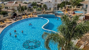 A large, curved swimming pool with multiple lanes, surrounded by palm trees and sun loungers. - Relaxing Getaway Awaits! Comfortable 1BR with Kitchen & Balcony, 2 Onsite Pools! (Albufeira)