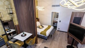 Une chambre d’hôtel moderne équipée d’un lit, d’une télévision, d’un coin repas avec une table et des chaises, et d’un petit coin cuisine.