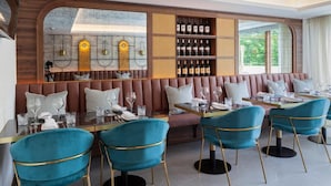 A restaurant with a long counter, teal chairs, and a wine rack.