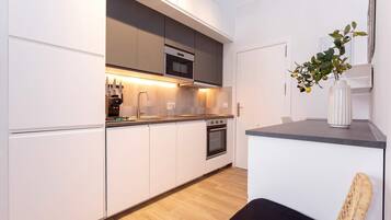 Une cuisine moderne avec des meubles blancs, un four en acier inoxydable et un plan de travail noir.