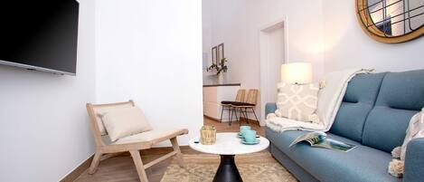 Un salon moderne avec un téléviseur à écran plat, un canapé bleu, une table basse ronde et une chaise en bois.