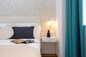 A neatly made bed with pillows, a bedside table with a lamp, and a wall with floral wallpaper. - Cozy Apartment in Center of Seville. Pajaritos IV (Seville)