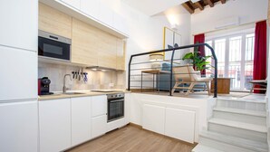 A modern kitchen with white cabinetry, a built-in oven, and a microwave. There is a staircase leading to a balcony with a red curtain and a potted plant. - Luxury Apartment in Sevilla Center. Pajaritos V (Seville)
