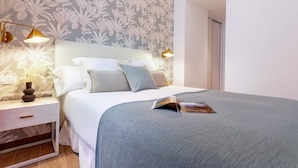 A neatly made bed with a grey blanket and pillows, a bedside table with a lamp, and a floral wallpaper. - Luxury Apartment in Sevilla Center. Pajaritos V (Seville)