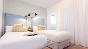 Una habitación de hotel con dos camas, una mesita de noche, una lámpara y una ventana con cortinas.