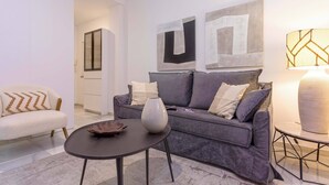 A modern living room with a grey sofa, a small round table, and a decorative vase. There are abstract paintings on the wall and a lamp on a side table. - Cozy Apartment in Sevilla Center. Baños IV (Seville)