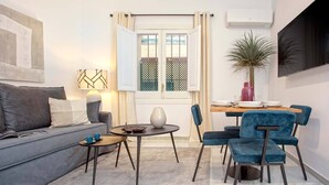 A modern living room with a sofa, coffee table, and chairs, a dining table with chairs, a potted plant, and a TV mounted on the wall. - Cozy Apartment in Sevilla Center. Baños IV (Seville)