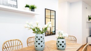 A dining table with two heart-patterned vases, wicker chairs, a white wall, a shelf with plants, and a mirror. - Modern Apartment in Prime Location. Marín García III (Málaga)