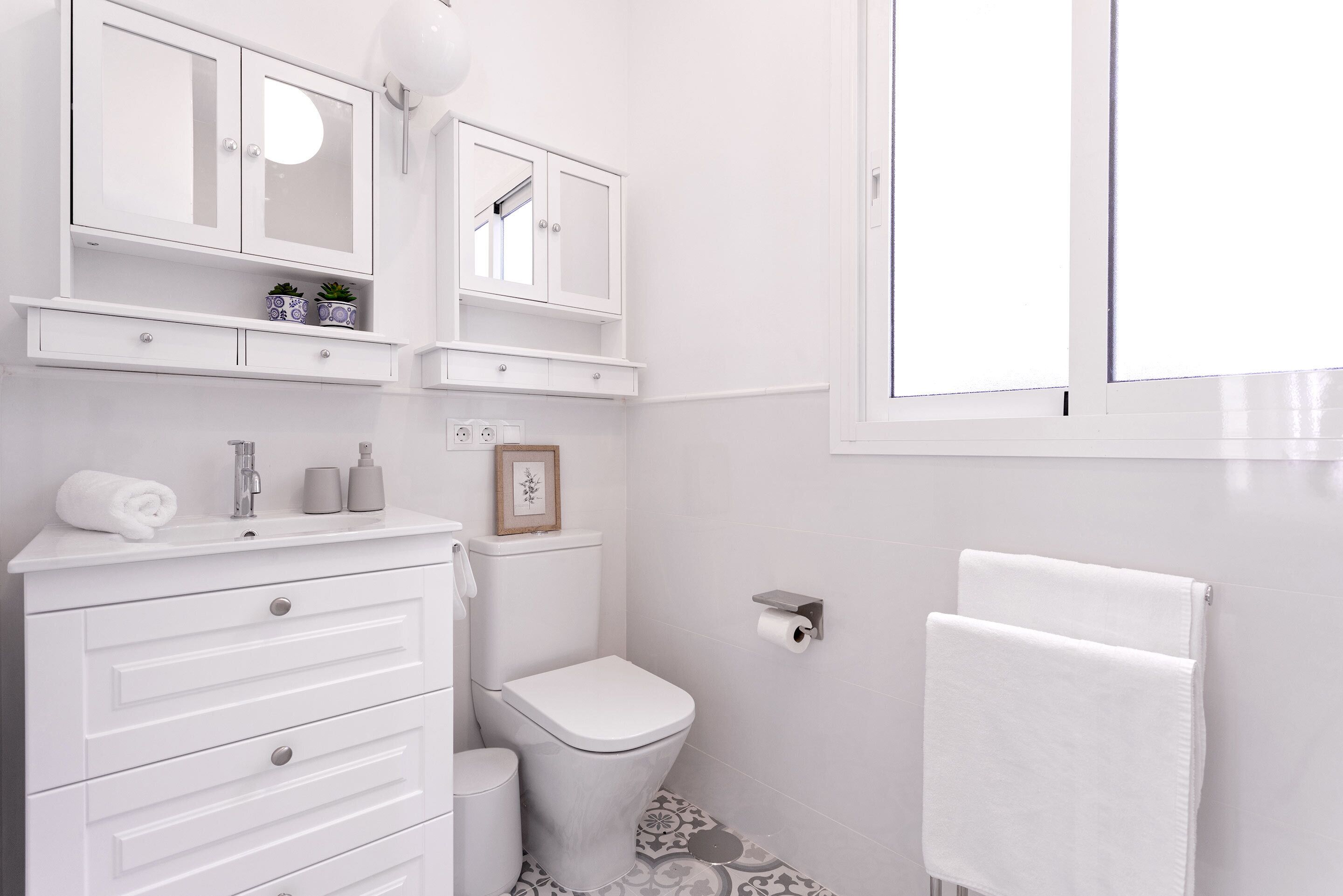 A modern bathroom with a white vanity, a toilet, and a towel rack.