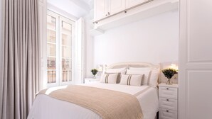Un dormitorio ordenado con una cama grande, una mesita de noche, un aparador y una ventana con cortinas.