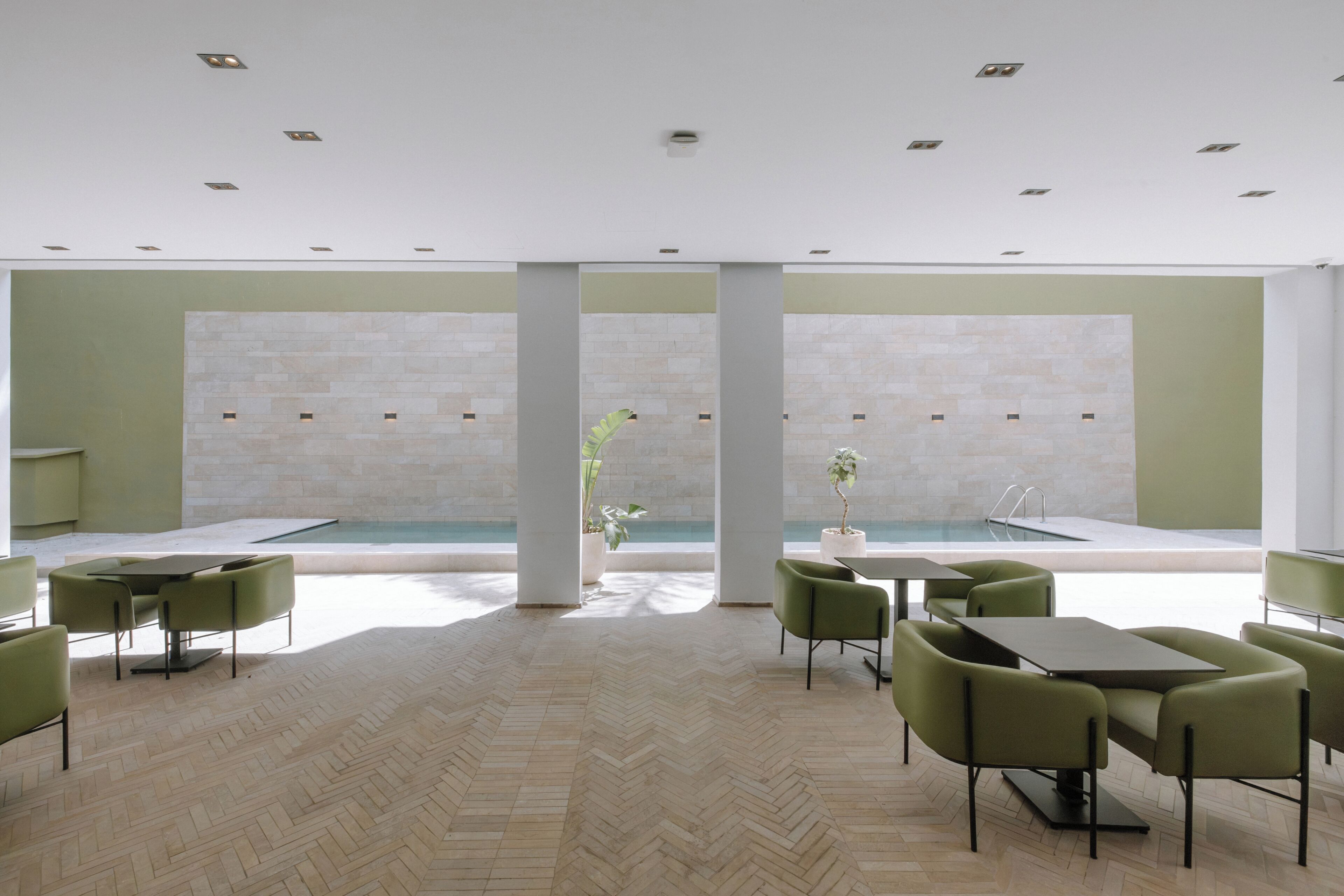 A modern indoor space with a pool, green chairs, and tables.