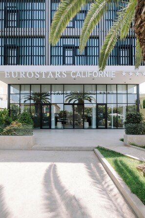 L’entrée de l’hôtel Eurostars California, avec sa façade moderne, ses palmiers et un ciel dégagé.