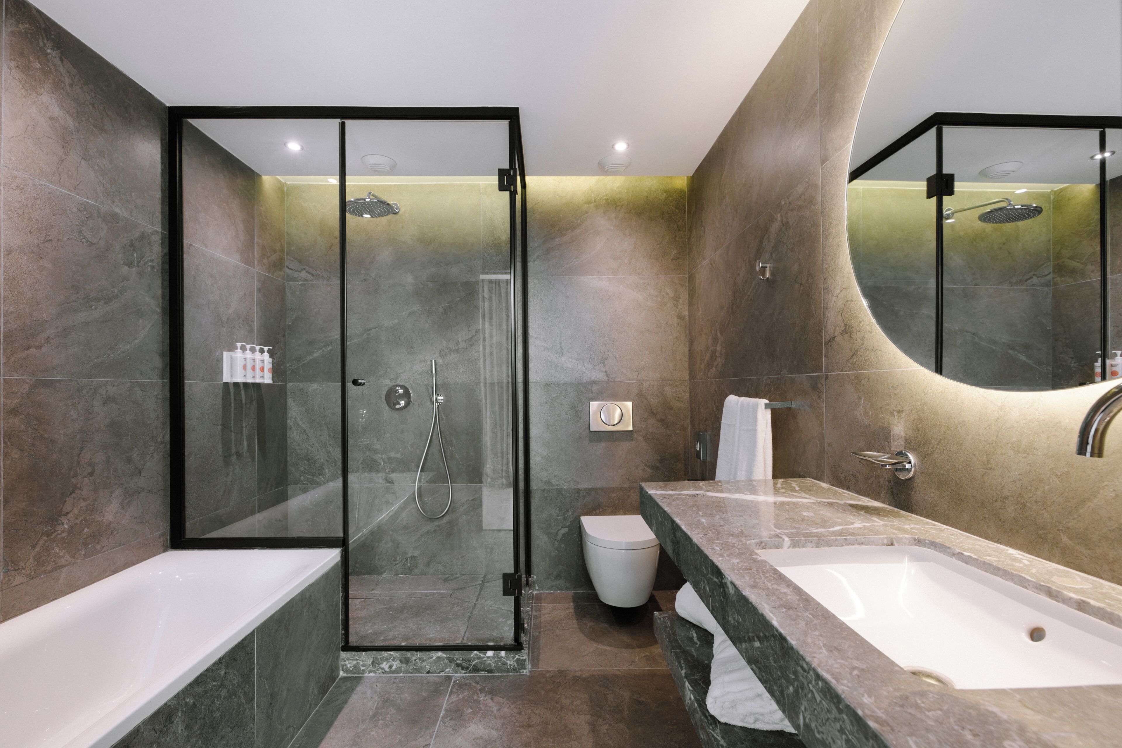 Un baño moderno con ducha envuelta en cristal, inodoro blanco y tocador de mármol con lavamanos.