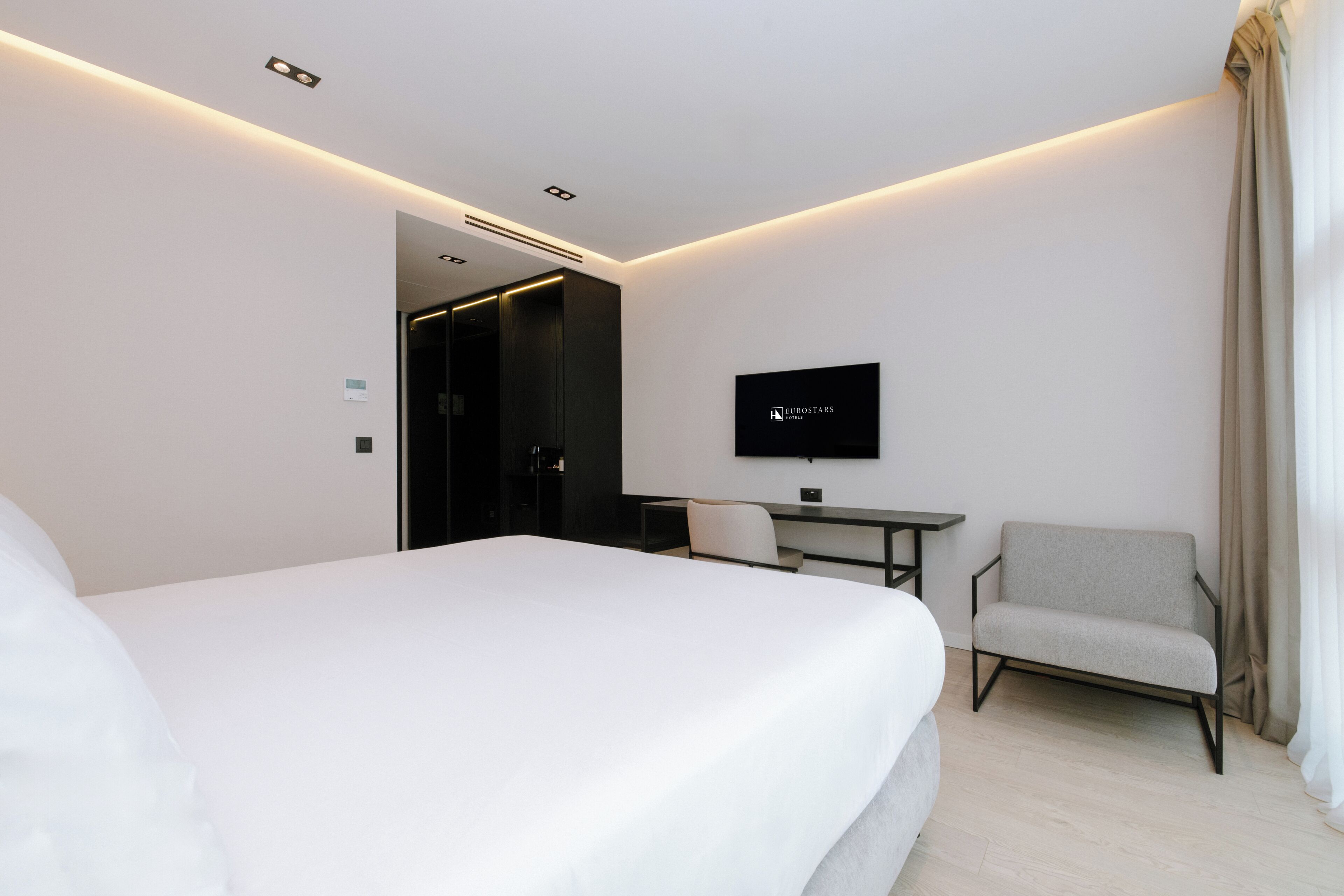 A hotel room with a bed, a desk, a chair, a television, and a door leading to another room.
