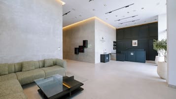 Un hall d’entrée moderne comprenant un canapé, une table basse en verre, un comptoir d’accueil et un panneau d’information fixé au mur.