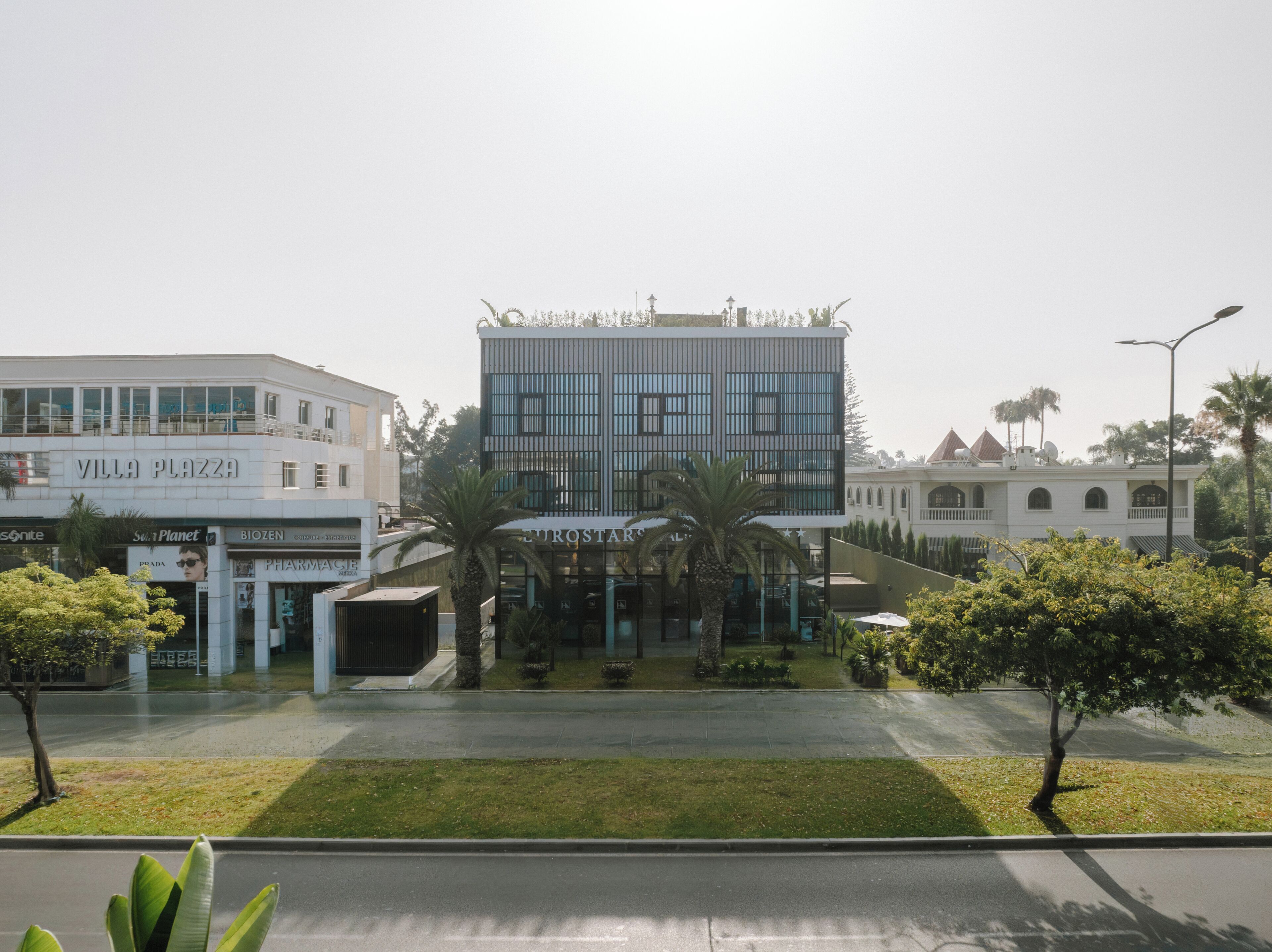 A modern building with a glass facade, surrounded by palm trees and a well-maintained lawn.