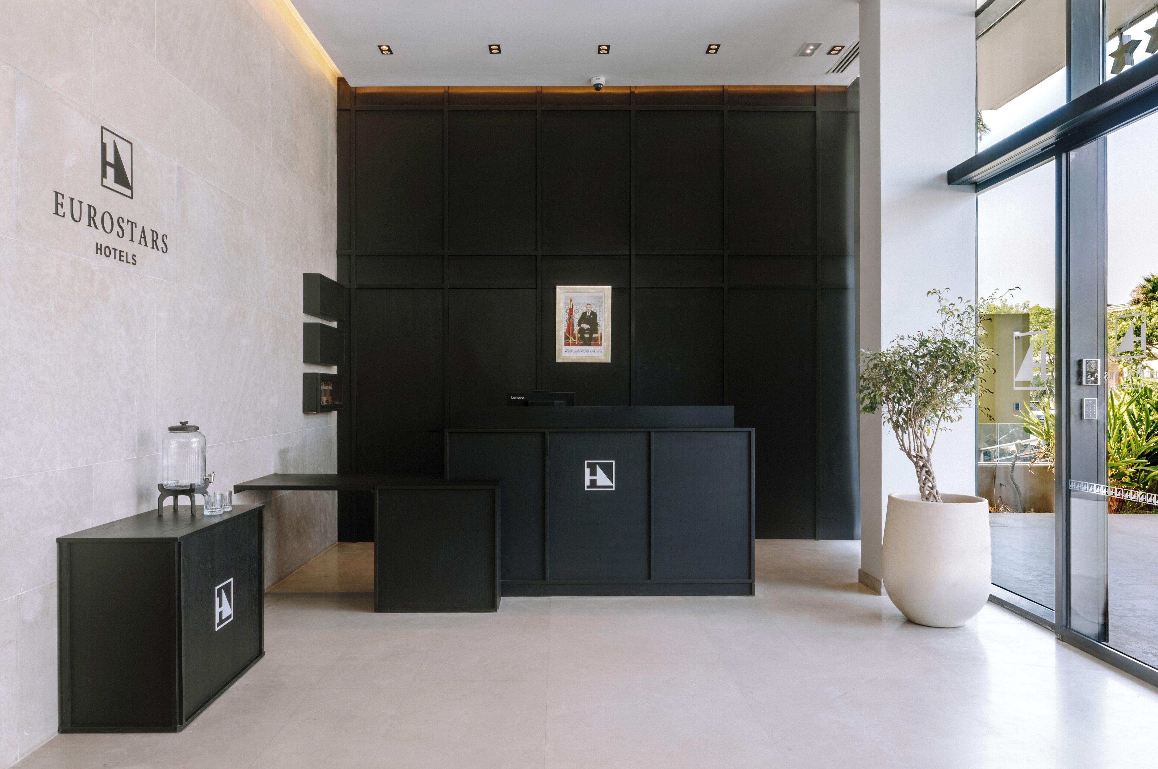 A reception area with a modern design, featuring a reception desk, a framed photograph on the wall, and a potted plant.