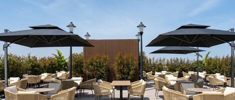 An outdoor seating area with tables and chairs, umbrellas, and street lamps.