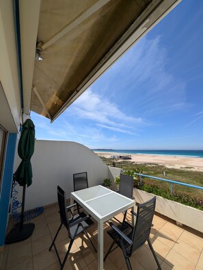 A balcony with a table and chairs, overlooking a beach.
