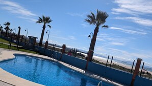 A swimming pool with a tiled deck, surrounded by palm trees and a fence. - 182 Livingtarifa Famara (Tarifa)