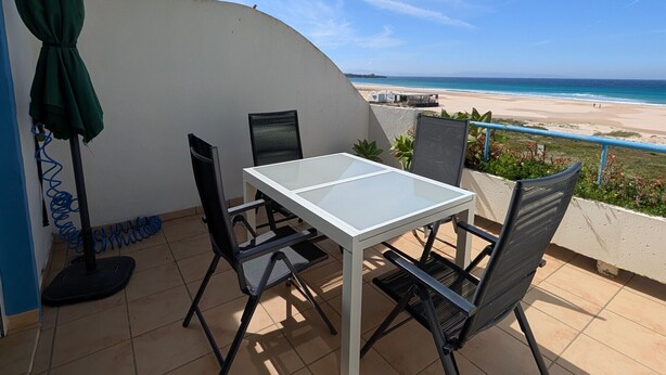 A patio with a table and chairs, a green umbrella, and a view of the beach. - 182 Livingtarifa Famara (Tarifa)