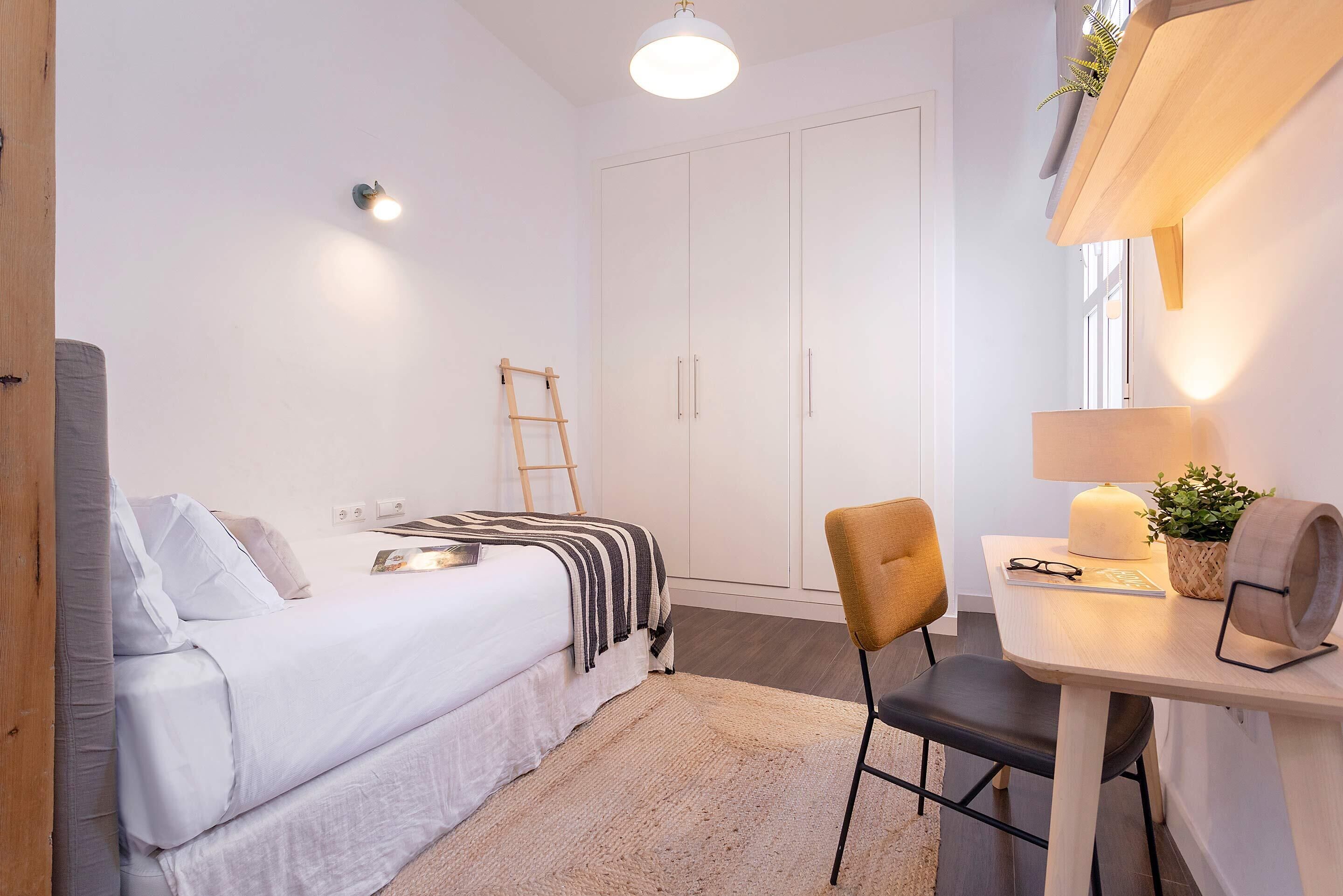 A bedroom with a bed, bedside table, lamp, chair, and wardrobe.