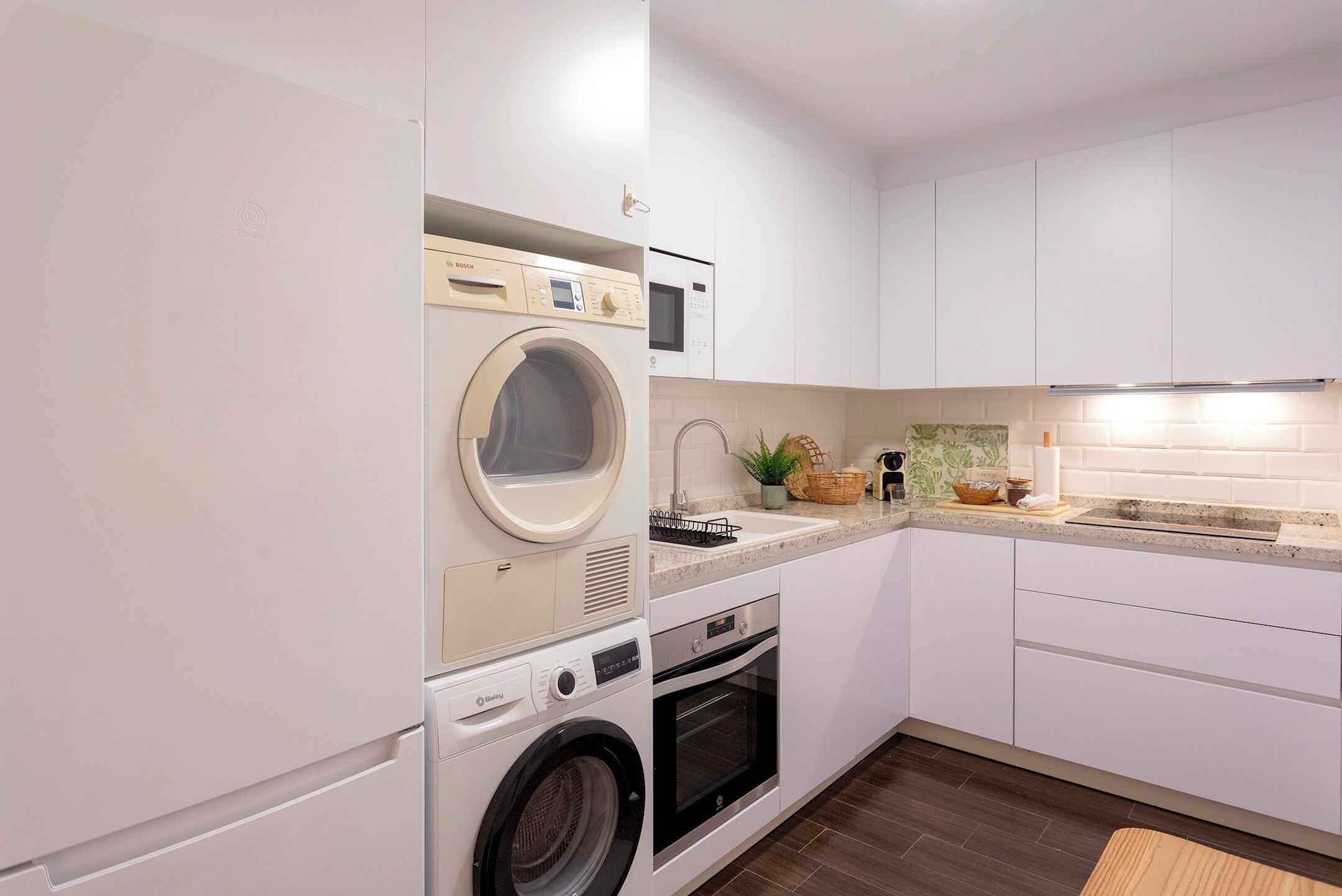 Une cuisine compacte équipée d’un lave-linge, d’un four, d’un four à micro-ondes et d’un évier sur lequel est posée une plante.