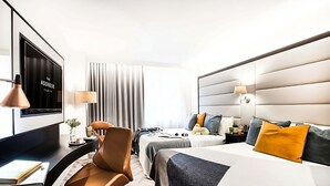 Een hotelkamer met een bureau, twee bedden, een televisie, een lamp en een raam met gordijnen.