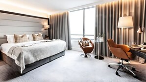 Ein modernes Hotelzimmer mit einem großen Bett, einem Schreibtisch, einem Stuhl und einem großen Fenster mit Vorhängen.