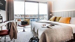 Ein Hotelzimmer mit einem großen Bett, einem Schreibtisch, einem Stuhl und Blick auf die Stadt.