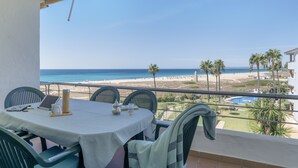Een balkon met een tafel en stoelen, met uitzicht op een strand en zwembad.