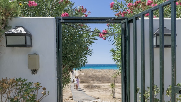 Een pad dat naar een strand leidt, met een poort, plantenbakken en een lantaarnpaal.