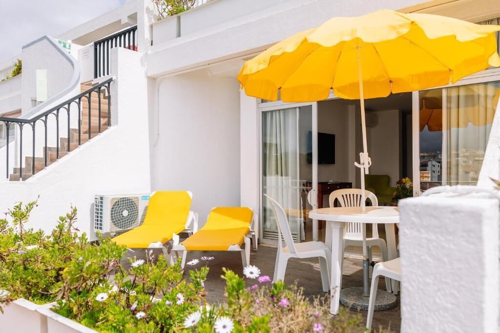 Ein Balkon mit gelben Stühlen, einem Tisch und einem gelben Sonnenschirm.