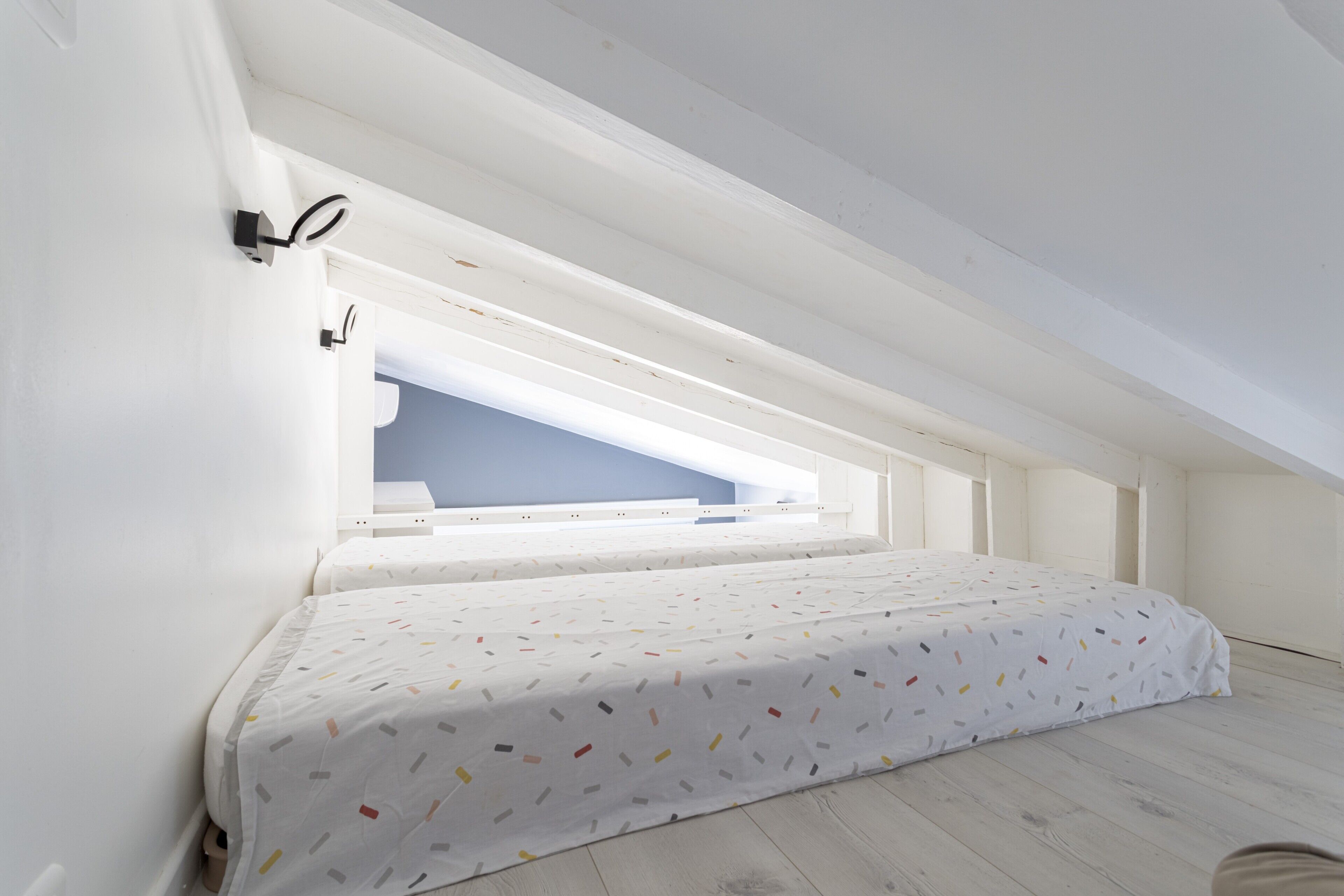 Un dormitorio con techo inclinado, una cama con colcha estampada y un tragaluz.
